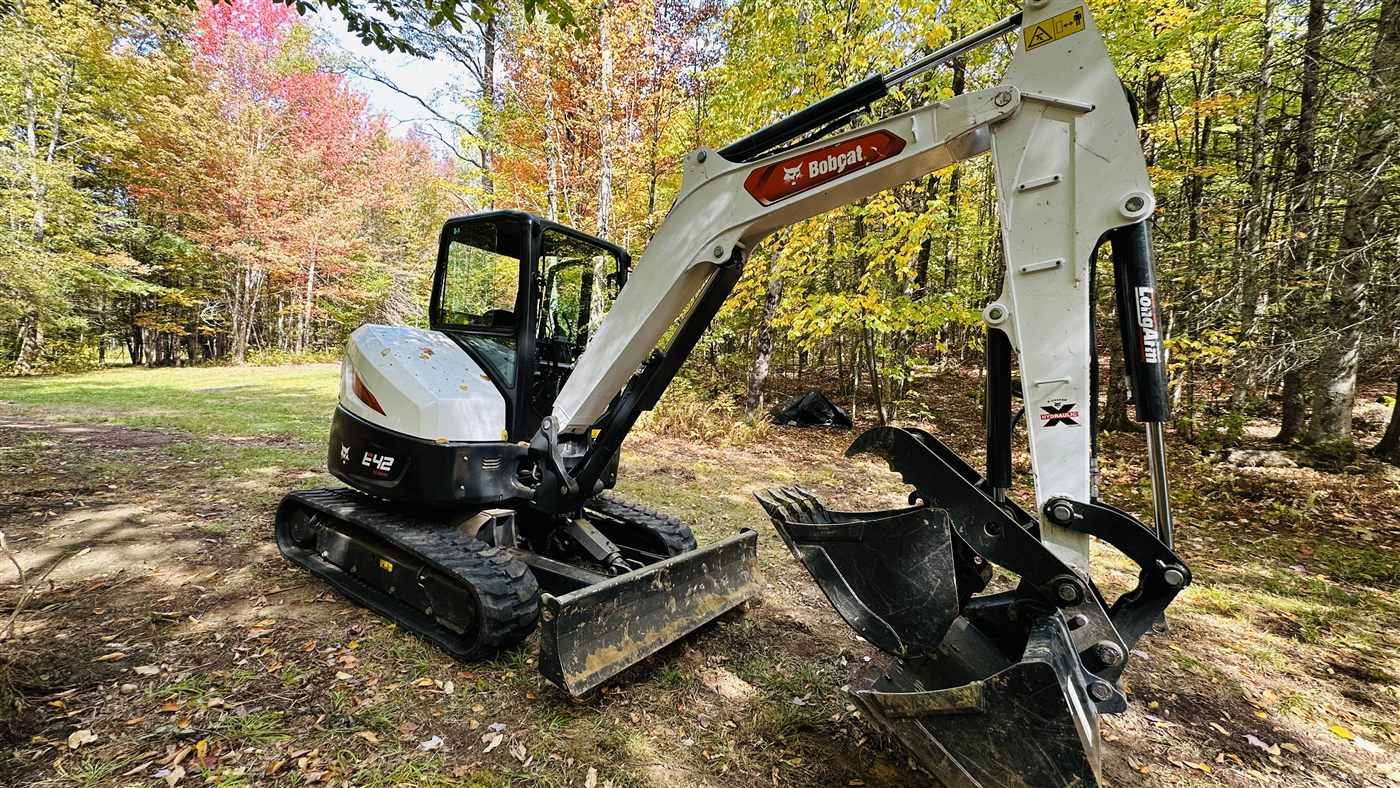 Excavator bucket working in a wooded excavation area